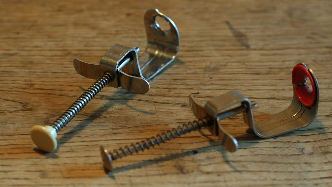 Two vintage metal cherry pitters with spring-loaded mechanisms and plastic-tipped plungers, resting on a wooden surface