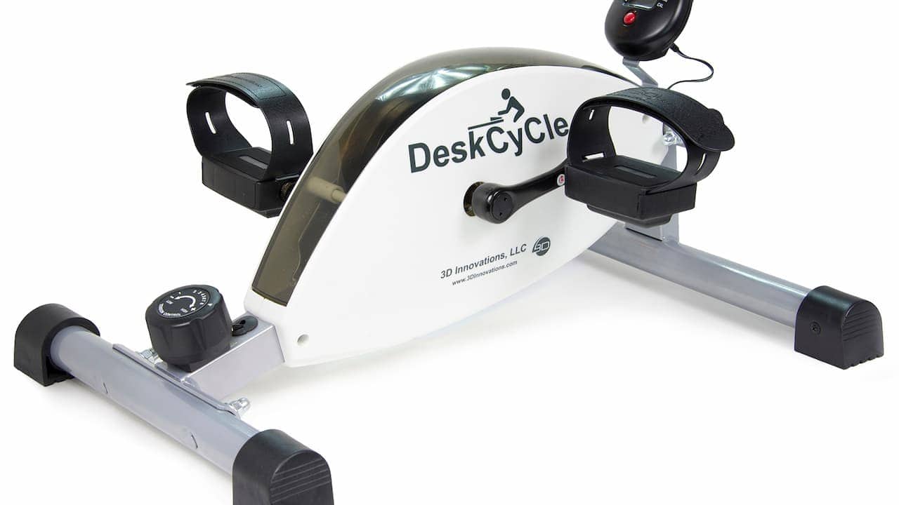 A compact under-desk exercise bike labeled “DeskCycle,” featuring two pedal straps, a resistance knob, and a small digital display attached by wire
