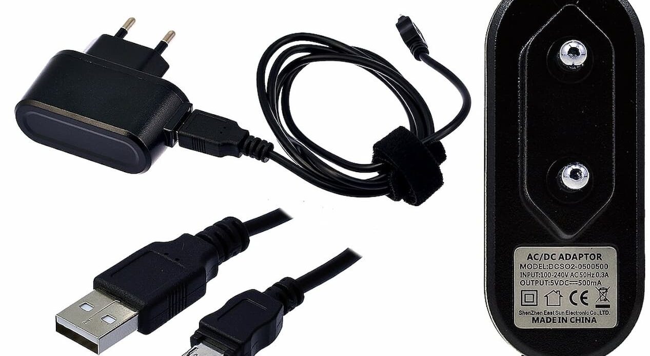 Set of electronic charging accessories including a USB wall adapter, USB-A to barrel plug cable, and a close-up of an AC/DC adaptor label on a white background