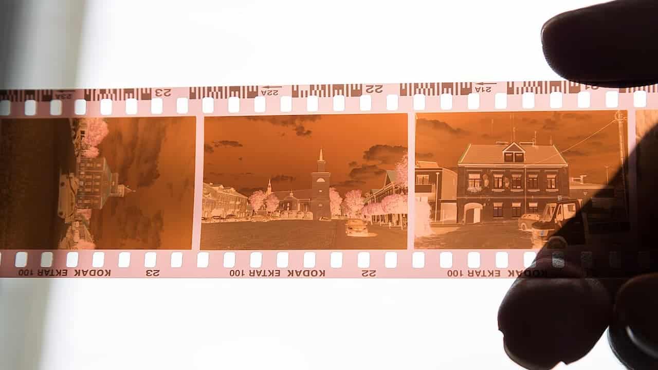  A strip of Kodak Ektar 100 film negatives held against a light source, showing three photographic frames with inverted colors and sprocket holes along the edges