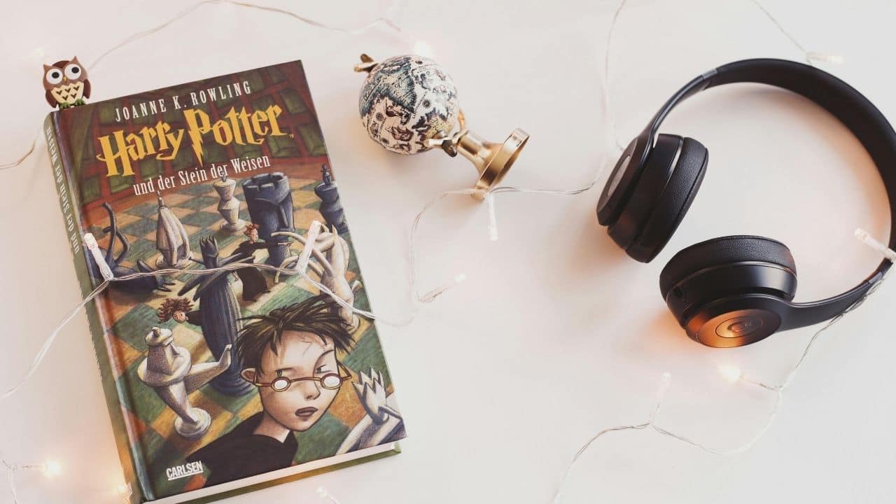 German edition of a Harry Potter book on white surface, surrounded by fairy lights, headphones, and decorative items