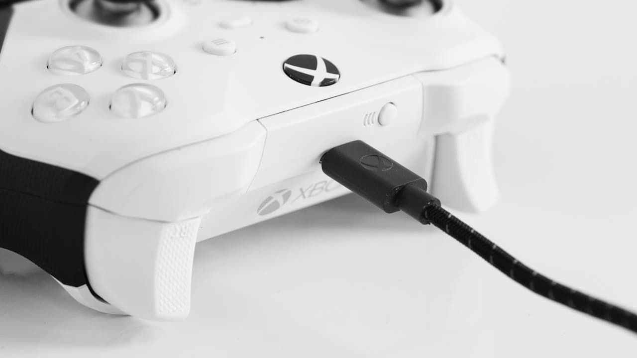  White Xbox controller with a braided USB charging cable plugged in, set against a white background