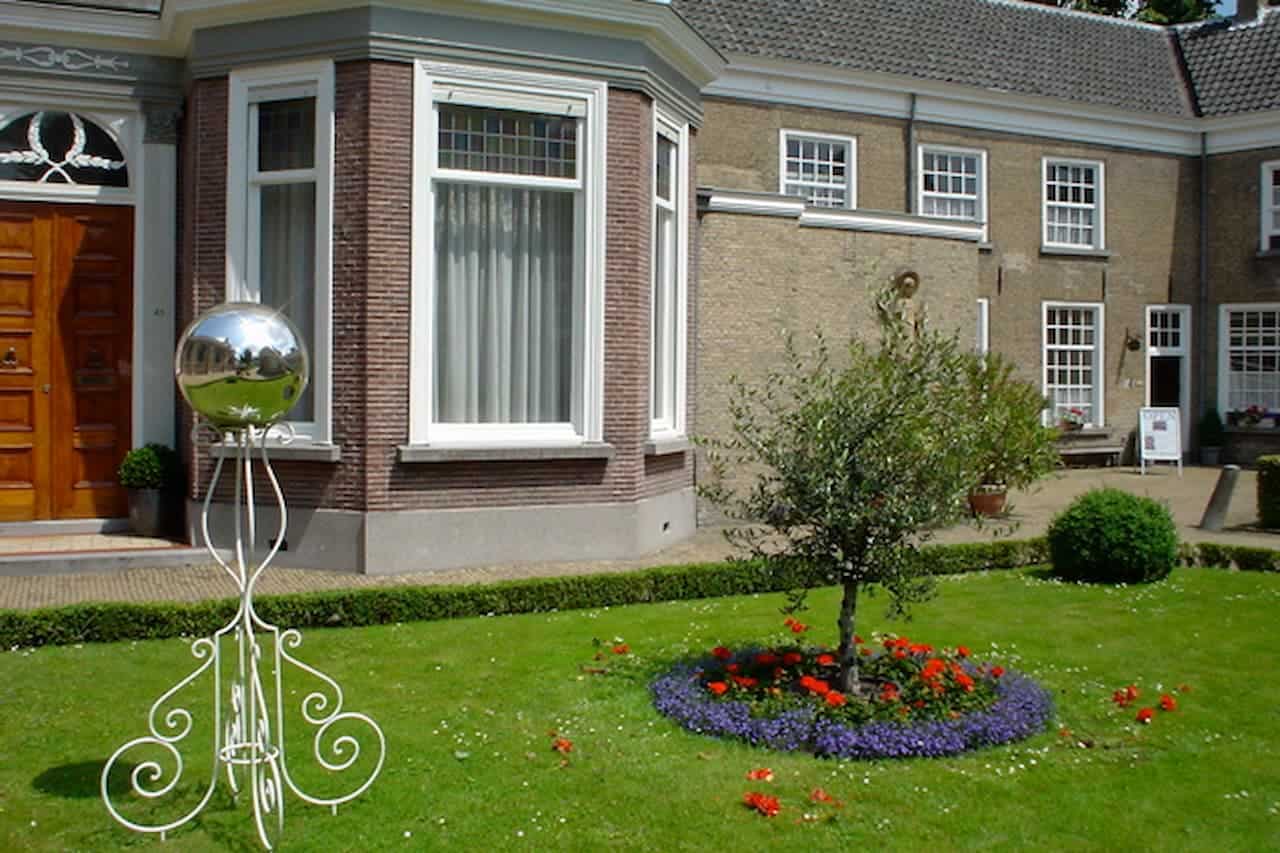 Elegant brick house with bay window, wooden door, manicured lawn, ornamental gazing ball, and circular flower bed with small tree