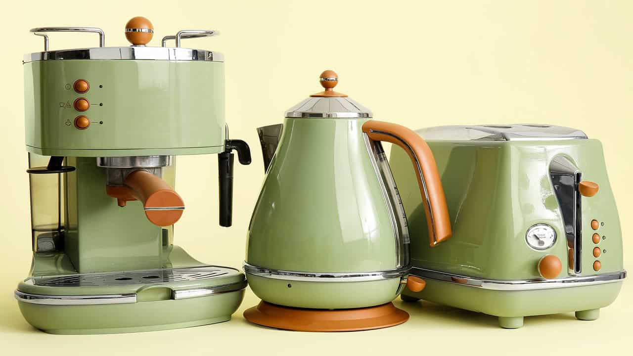 Set of matching green kitchen appliances including espresso machine, electric kettle, and toaster with copper accents