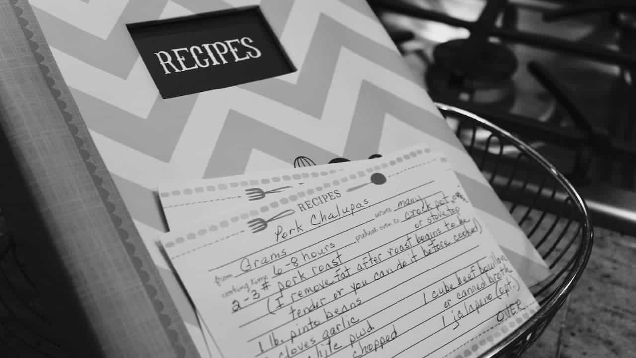 Black and white photo of handwritten recipe card for pork chops in wire basket, recipe box with chevron pattern in background