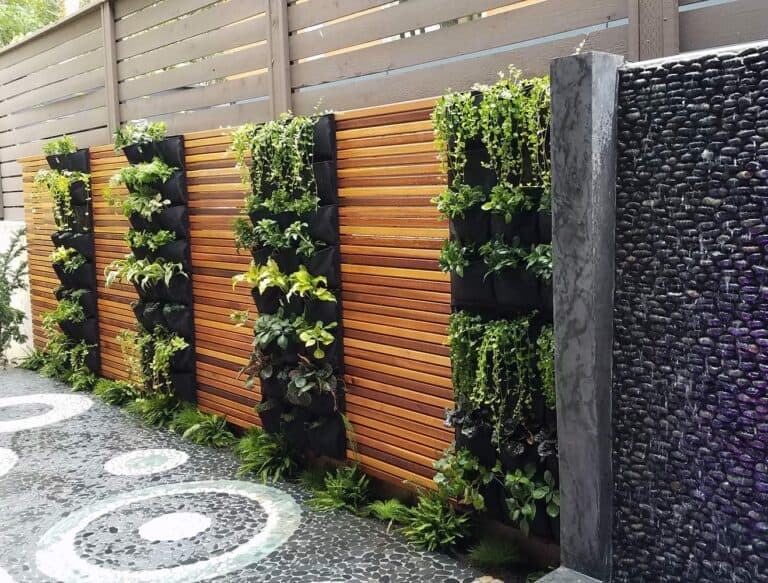 Modern garden wall featuring vertical plant pockets on wooden slat fence, black stone water feature, decorative pebble pathway with circular pattern