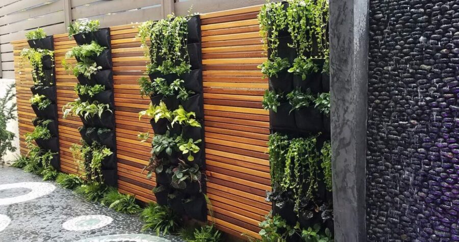 Modern garden wall featuring vertical plant pockets on wooden slat fence, black stone water feature, decorative pebble pathway with circular pattern