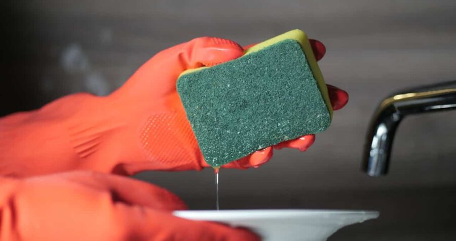 Person wearing orange rubber gloves holding a wet kitchen sponge
