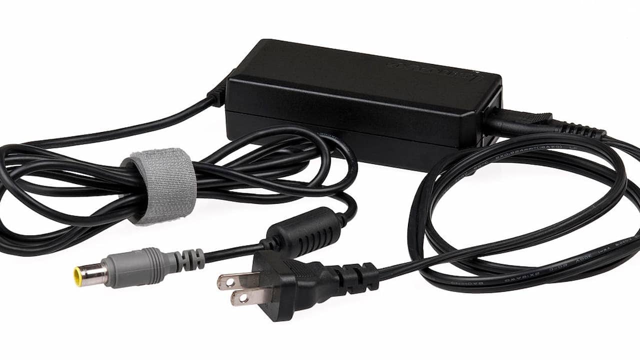 Black laptop power adapter with an attached AC plug and cylindrical DC connector, coiled cords secured by a gray Velcro strap, placed on a white background