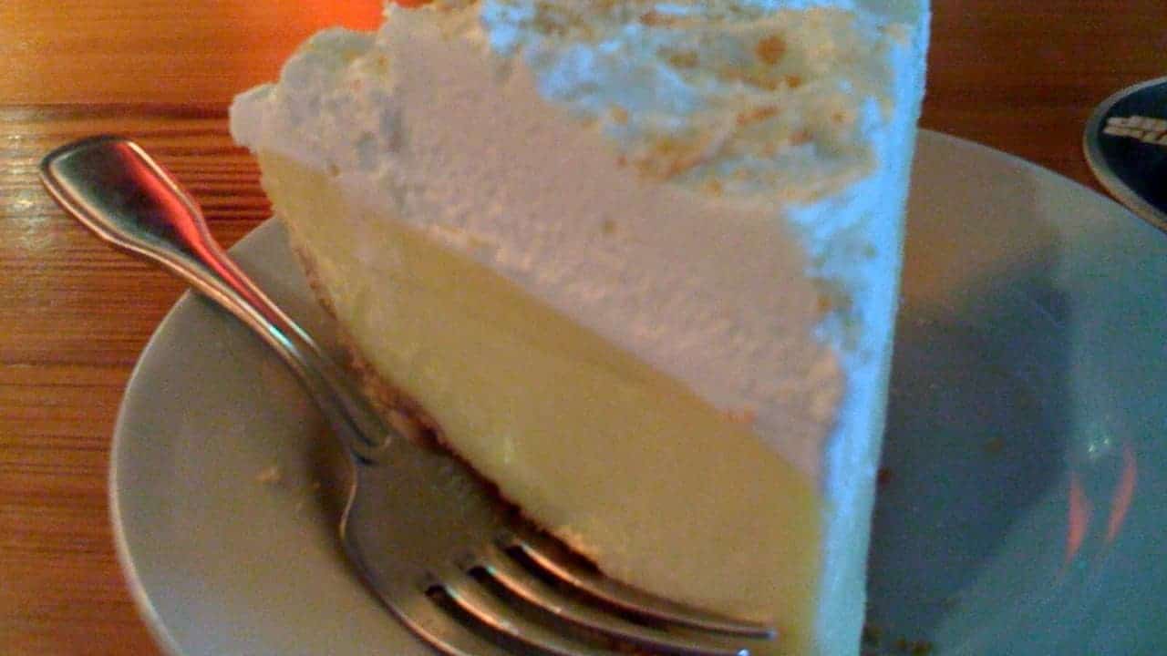 A slice of Lemon ice box pie on a white plate with a fork, served on wooden table