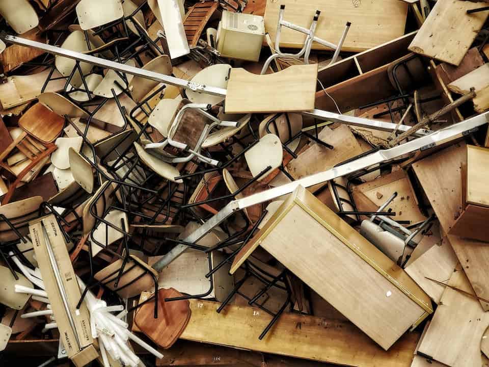 Large pile of broken and discarded wooden school desks with metal frames, chairs, and furniture parts in disarray