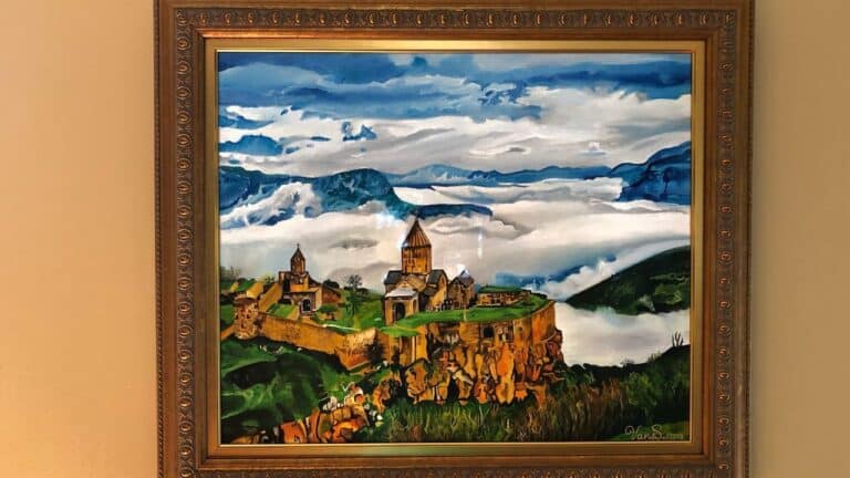 Framed oil painting depicting ancient monastery complex on mountainous landscape with dramatic cloudy sky and rolling green hills