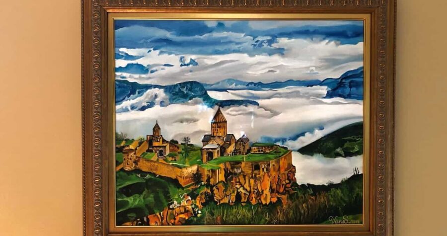 Framed oil painting depicting ancient monastery complex on mountainous landscape with dramatic cloudy sky and rolling green hills