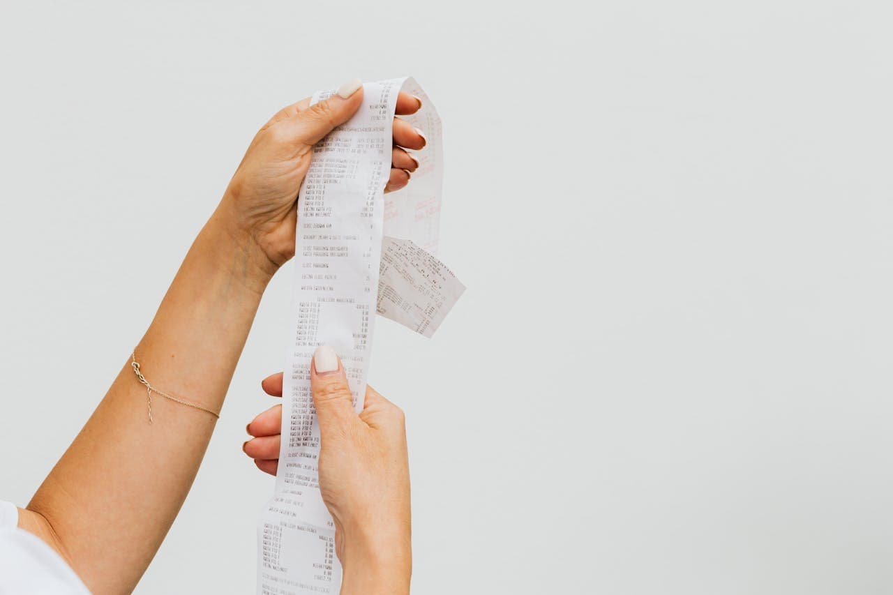 Person holding a long, printed receipt with multiple items listed, against a plain light background