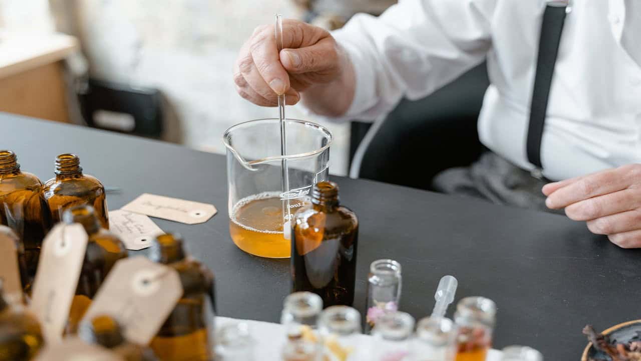 Hand stirring amber liquid in glass beaker with stirring rod, laboratory glassware on table