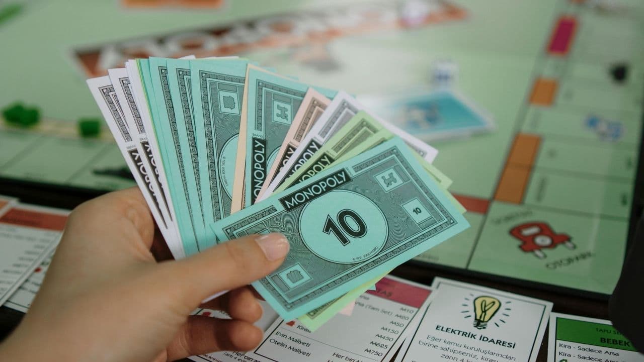 Hand holding Monopoly money in various denominations, Monopoly board in background