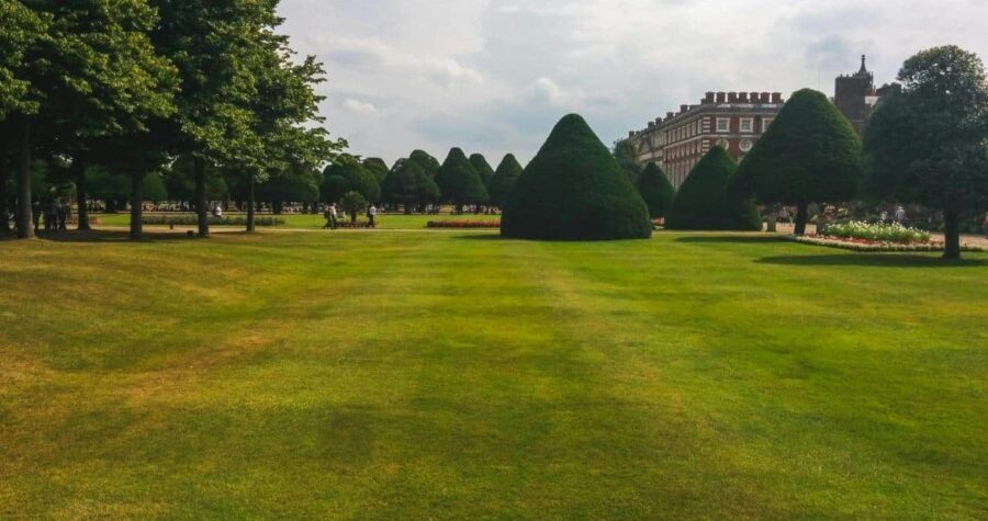 Large green lawn with trimmed hedges and trees in background, overcast sky above manicured grass field