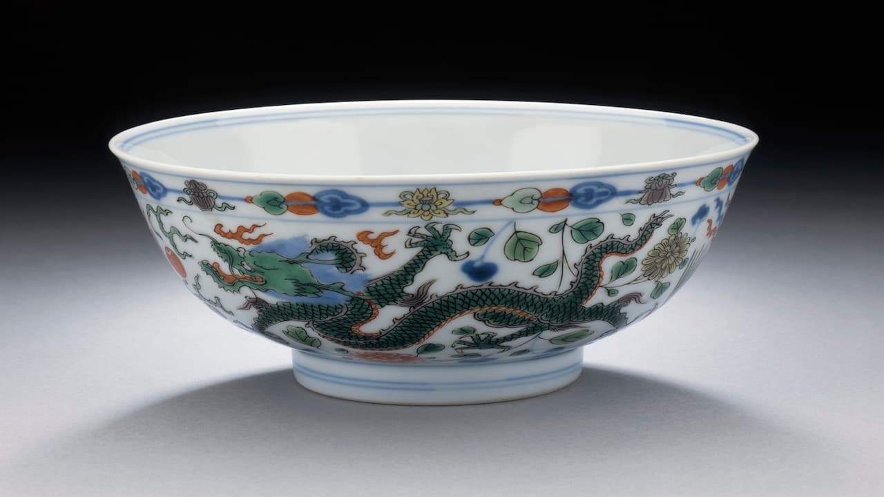 Porcelain bowl with intricate multicolored designs featuring a green dragon chasing a flaming pearl, surrounded by clouds