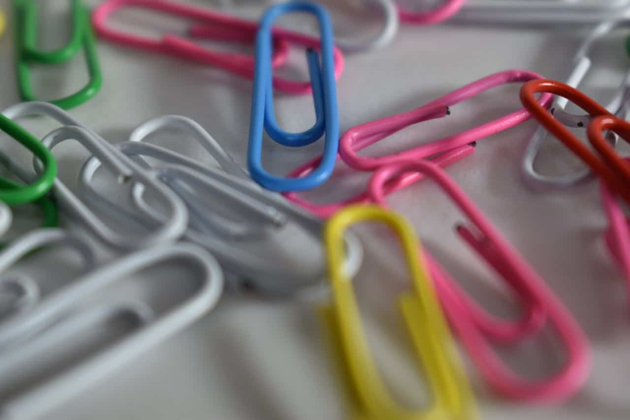 Close-up of assorted colorful paper clips scattered on a white surface, including blue, pink, yellow, green, white, and red clips