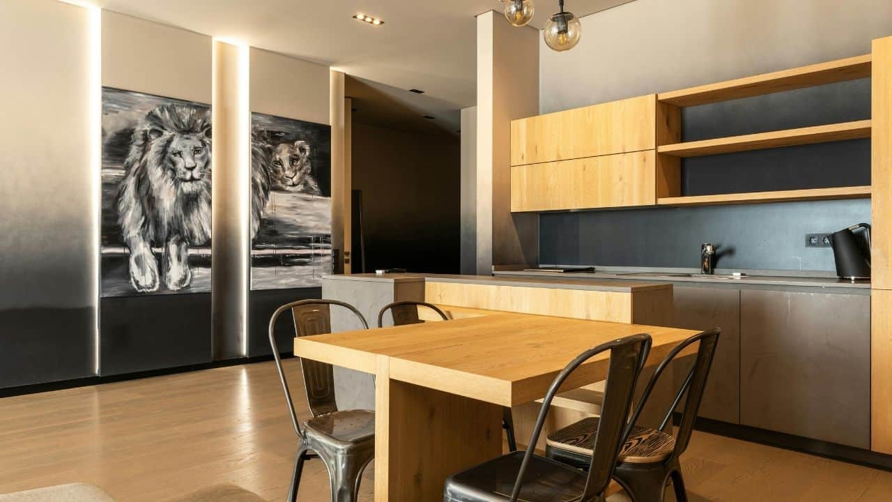 Modern kitchen and dining area with wooden table, dark chairs, yellow upper cabinets, white walls, and pendant lighting