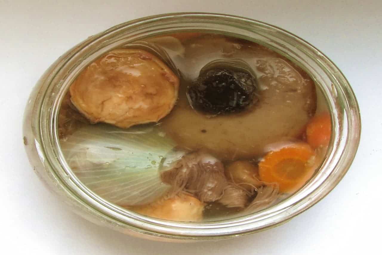 Top-down view of a glass jar filled with pickled vegetables and mushrooms