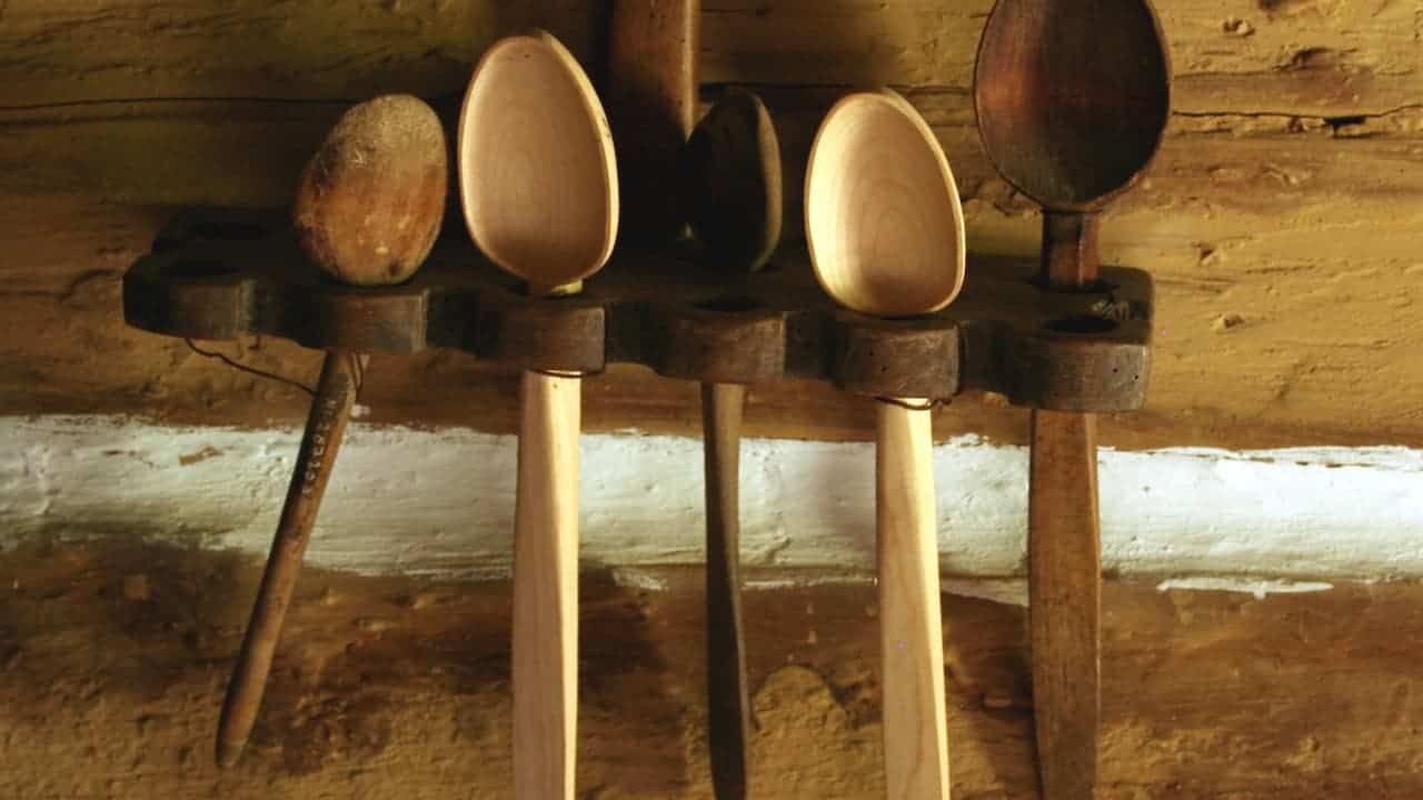 Traditional wooden kitchen utensils with carved bowls and long handles hanging on rustic log cabin wall in warm light