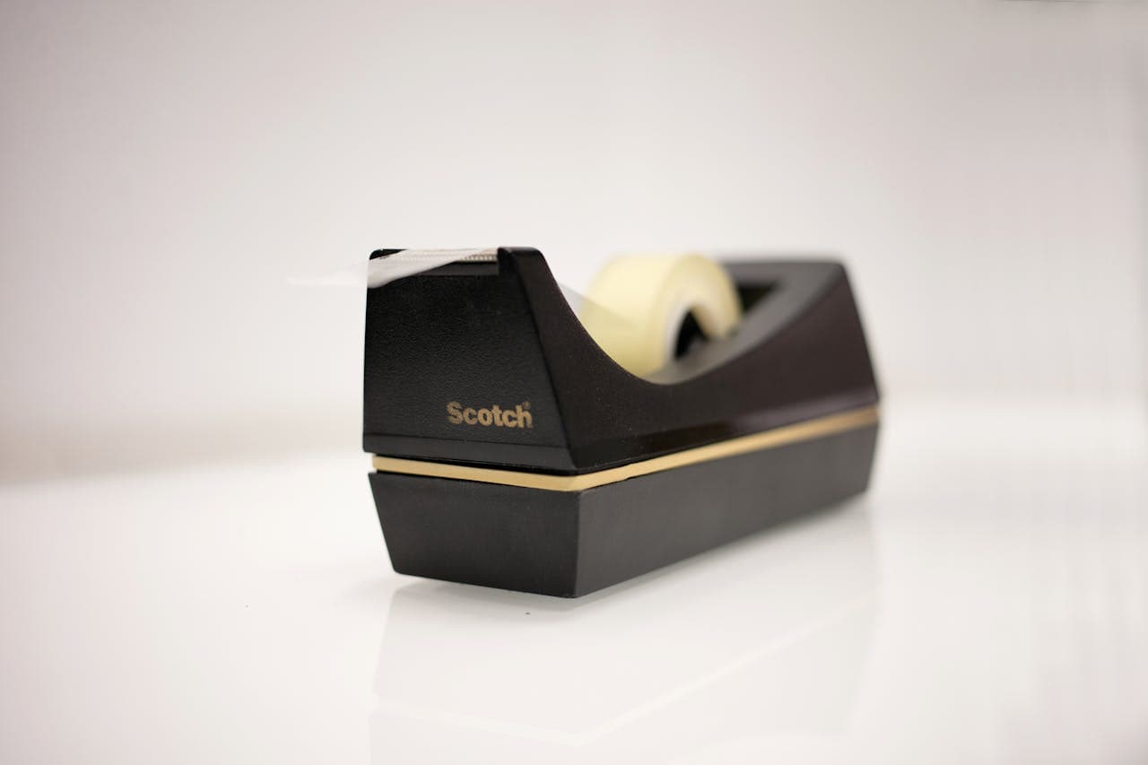 Black Scotch tape dispenser with a roll of clear tape, placed on a glossy white surface