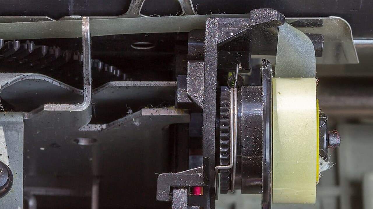 Close-up view of a typewriter correction tape mechanism, showing a yellow correction tape spool mounted within a metal and plastic assembly