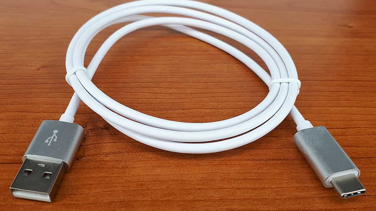 A coiled white USB-A to USB-C charging cable with metallic connectors, placed on a polished wooden surface