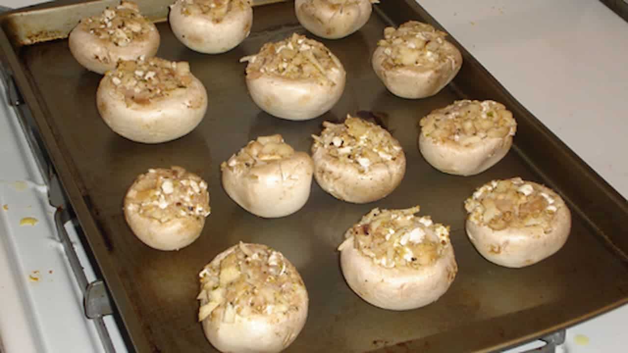 Stuffed mushroom caps filled with herb and cheese mixture arranged on dark baking sheet ready for cooking
