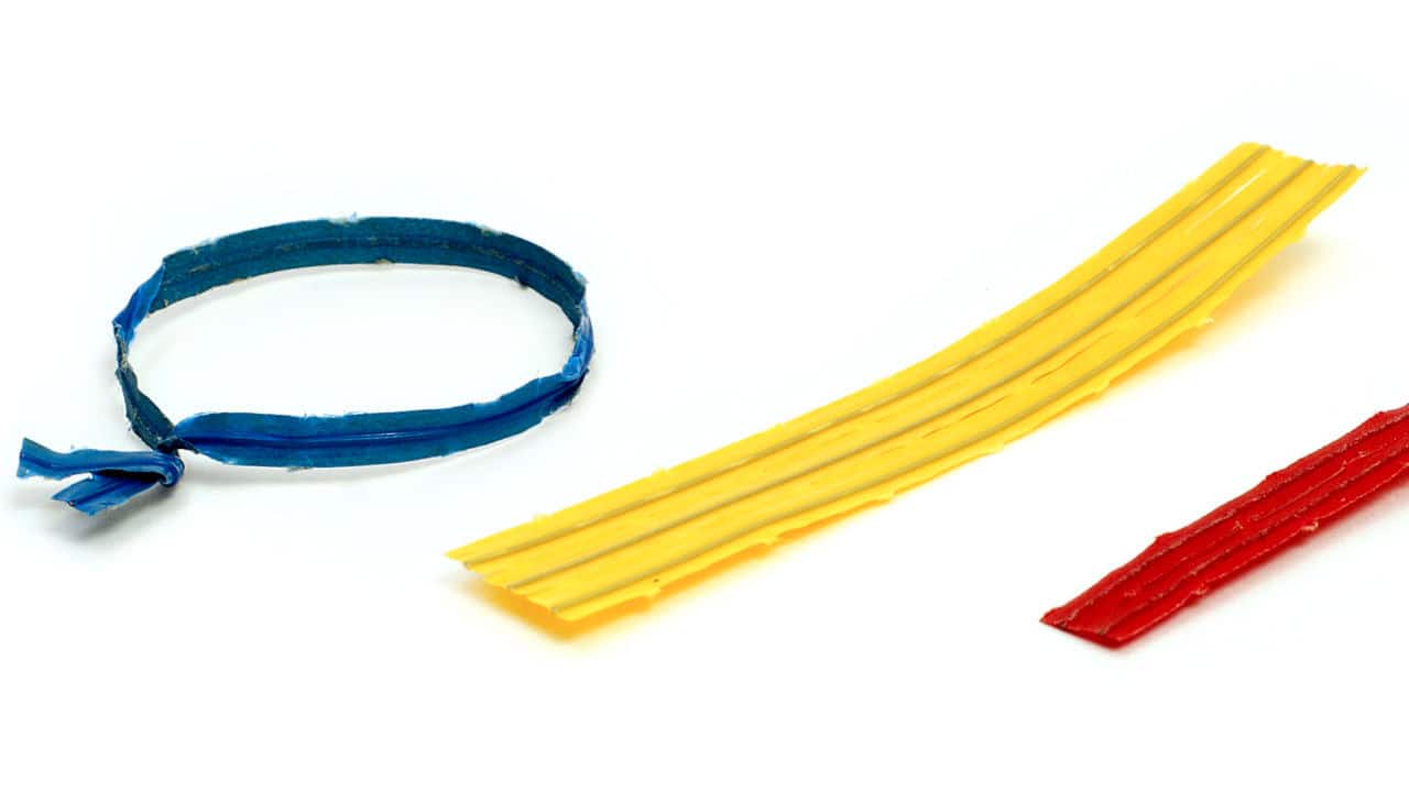 Three colorful used twist ties—blue looped, yellow flat, and red strip—on a white background