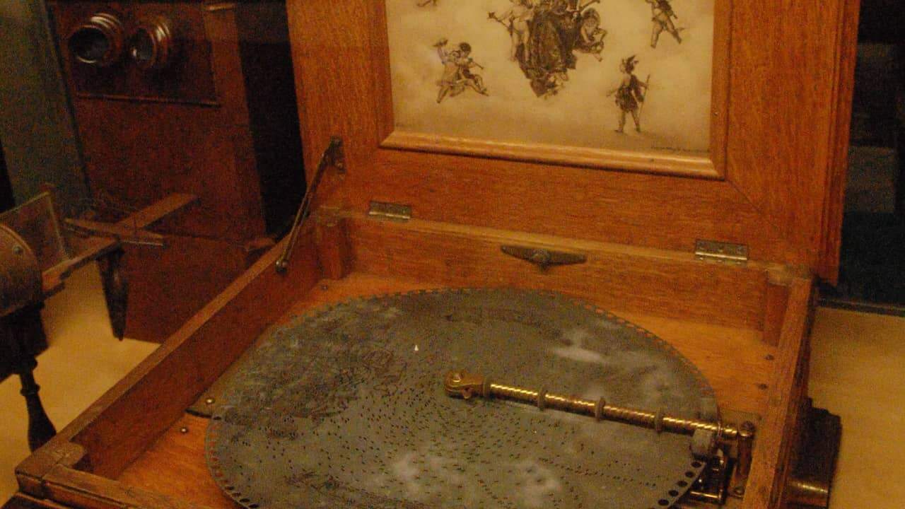 An open wooden music box with visible intricate interior details, polished wood finish, and a small metal winding key or mechanism inside