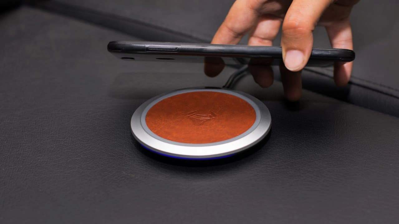 Hand placing a smartphone onto a round, leather-topped wireless charging pad on a dark leather surface