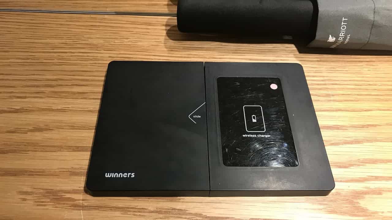 A black rectangular wireless phone charger labeled “winners,” placed on a wooden surface with a “slide” arrow pointing left and a Marriott umbrella partially visible at the top