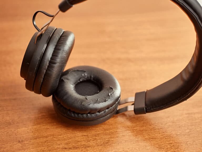 Close-up of black over-ear headphones with peeling and worn-out ear cushions placed on a wooden table