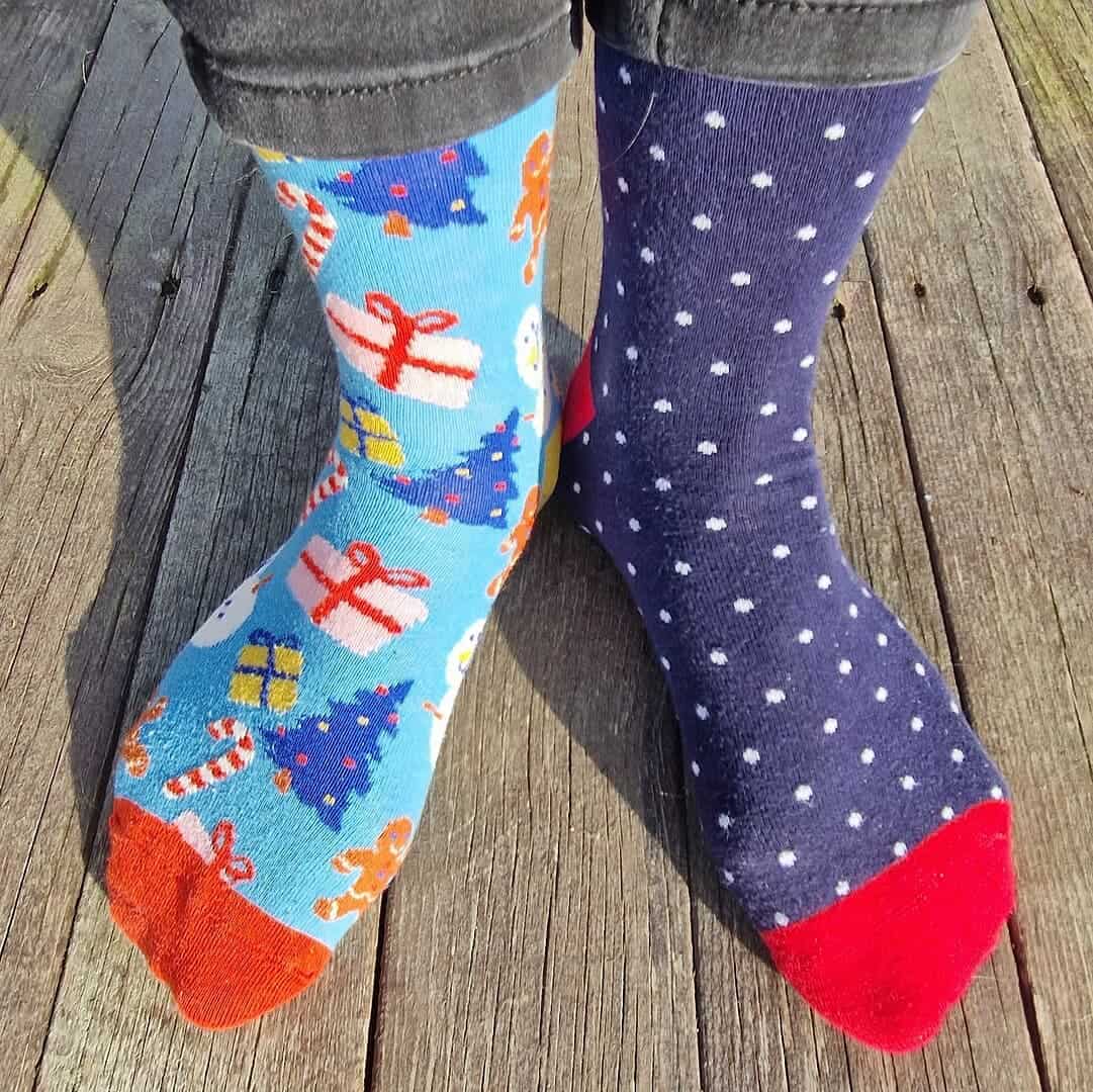 Mismatched socks on wooden floor, left sock blue with Christmas pattern, right sock navy with white polka dots, both with red toes