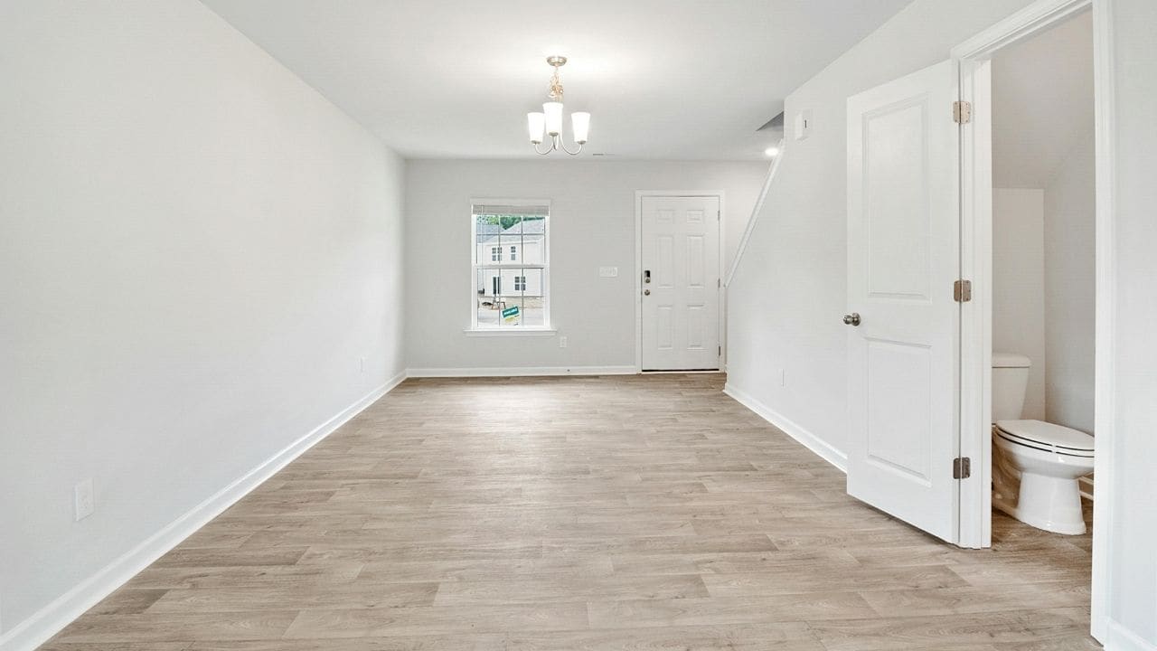 Clean, empty white room with light wood flooring, white walls, recessed ceiling lighting, and a window with white trim on the far wall