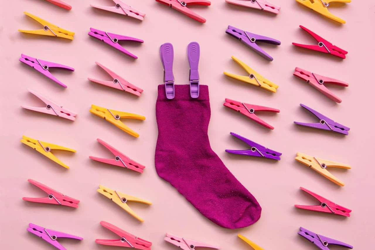Purple sock with two clothespins attached, surrounded by colorful pink, yellow, and purple clothespins on pink background