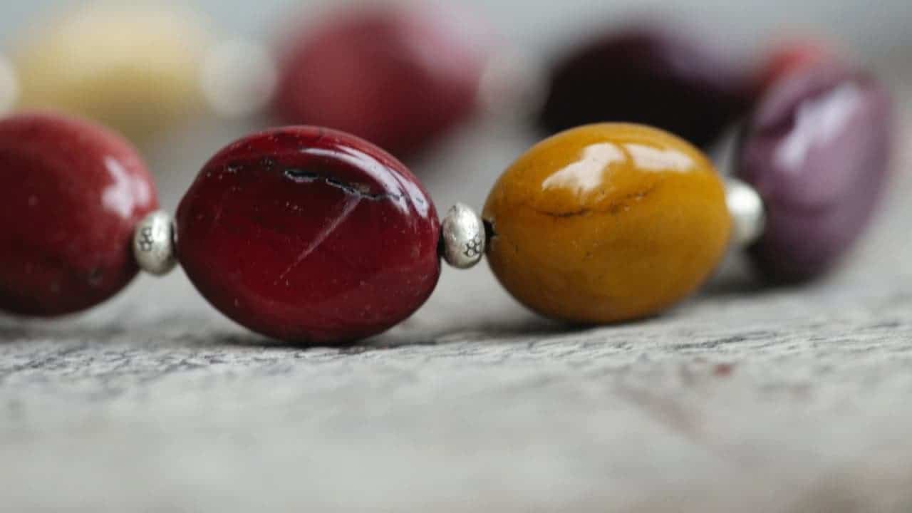 Polished gemstone beads in red and amber colors with silver spacers arranged on wooden surface, part of necklace