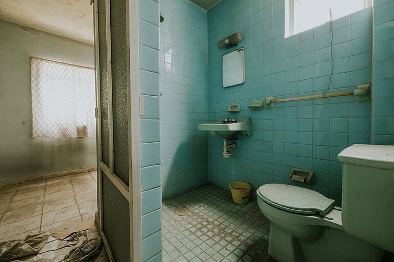 Retro Colorful Toilet and Sink with turquoise tile walls, white toilet, small sink, and adjoining room visible through doorway with textured glass