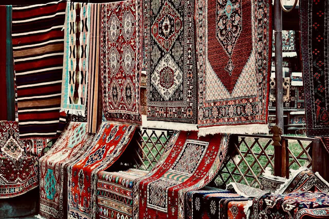 Bold geometric patterned rugs displayed at market stall, hanging and draped over wooden railings with intricate patterns