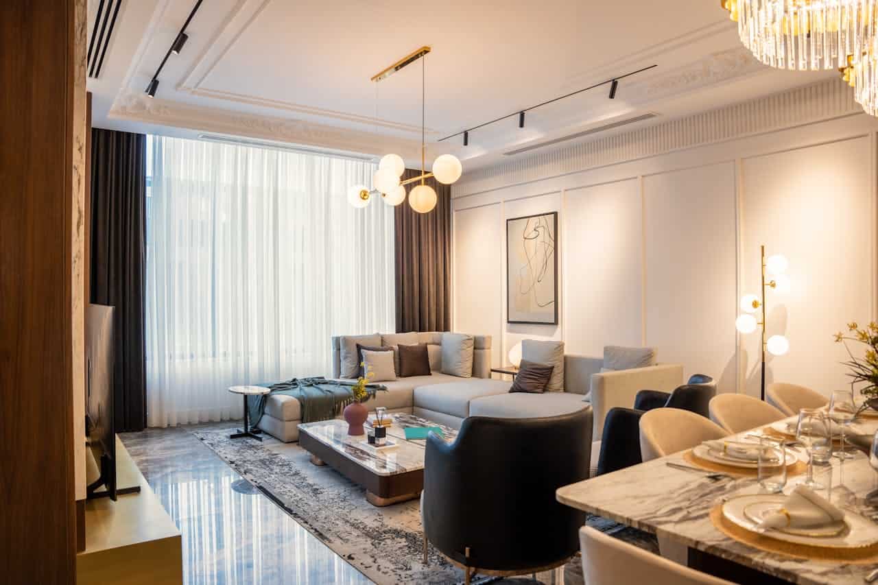 Elegant living and dining room with modern furniture, abstract art, chandelier, marble table, sectional sofa, and warm iconic mid-century lighting 