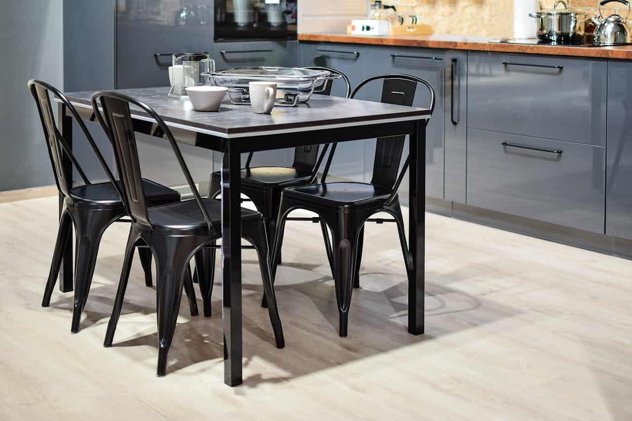 Modern dining area with black metal table and chairs, white cups, serving dish, and gray kitchen cabinets