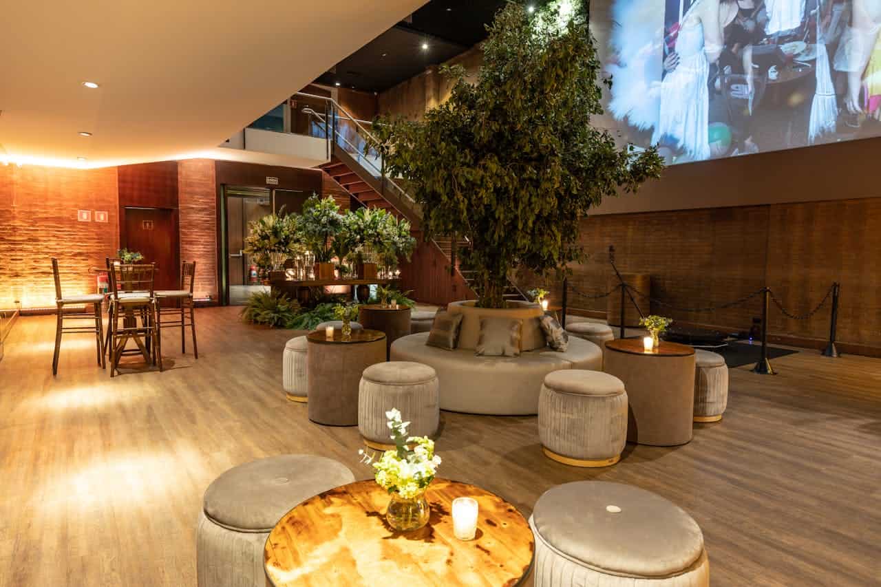 Elegant room with circular poufs seating around large tree, wooden floors, brick walls, projection screen, and ambient lighting