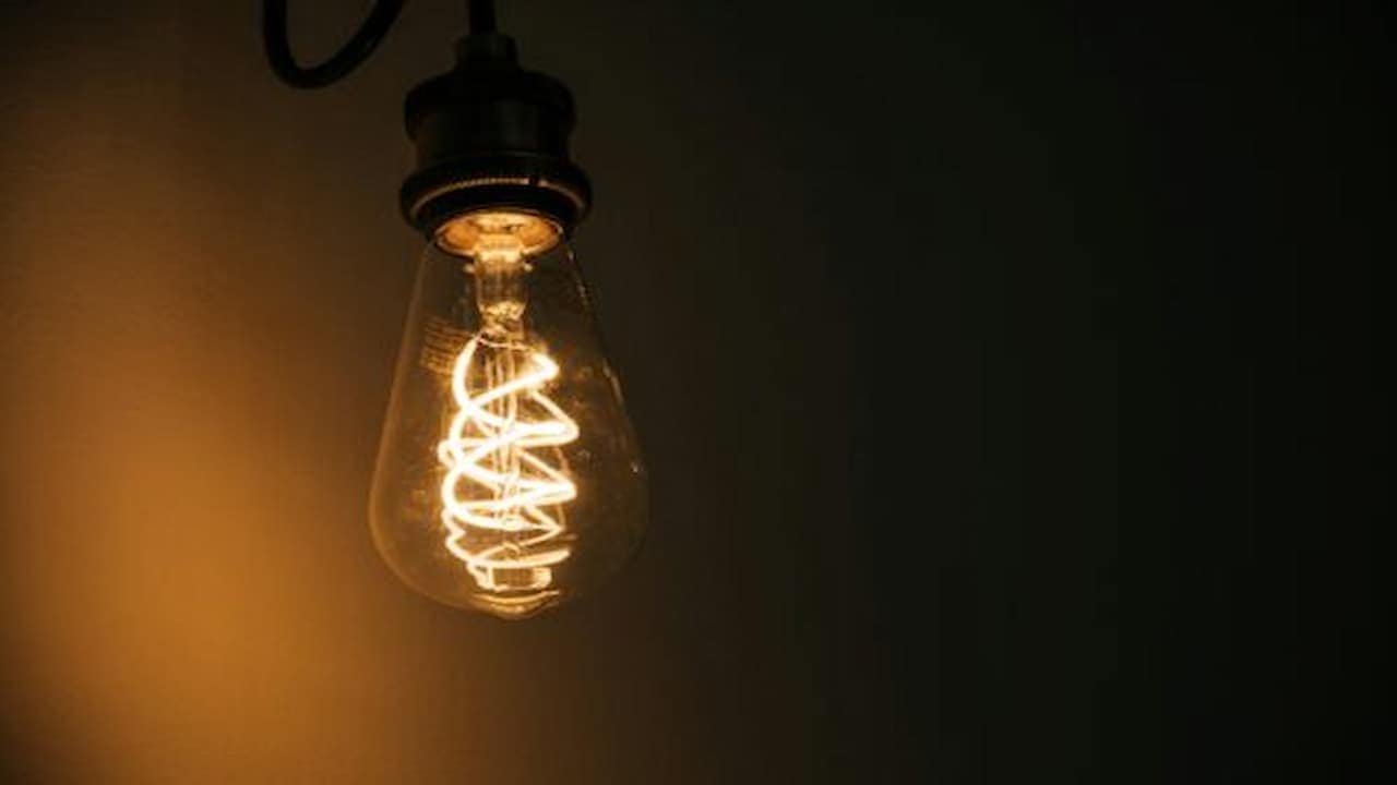 Close-up of a glowing vintage-style filament bulb, teardrop-shaped glass, suspended from a dark fixture