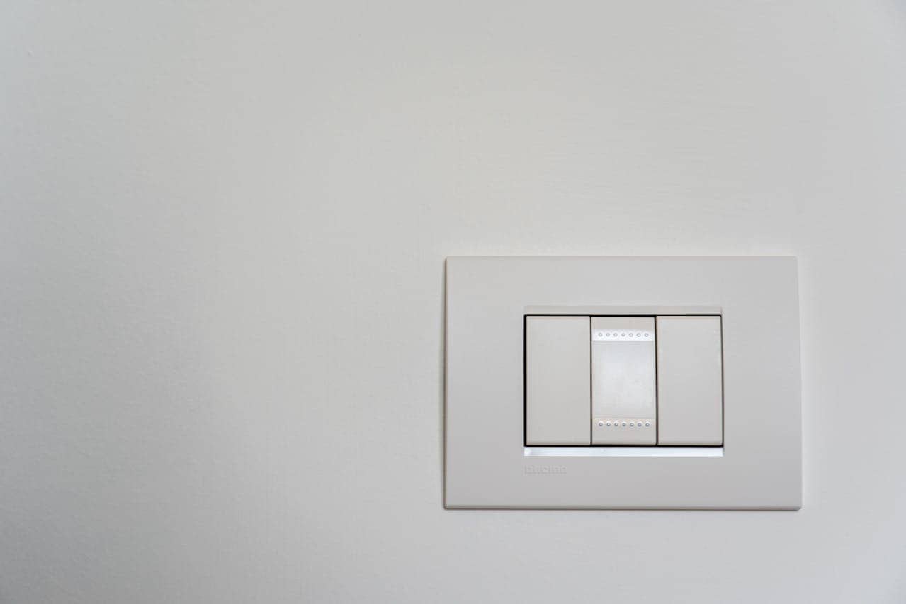 White rectangular light switch plate with three modern buttons mounted on a light gray wall