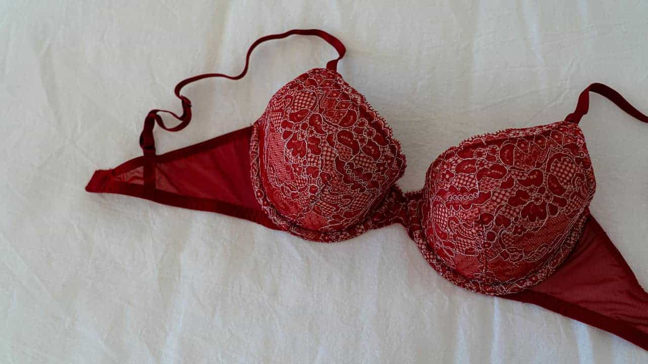 Red lace bra with floral detailing laid flat on a white fabric surface