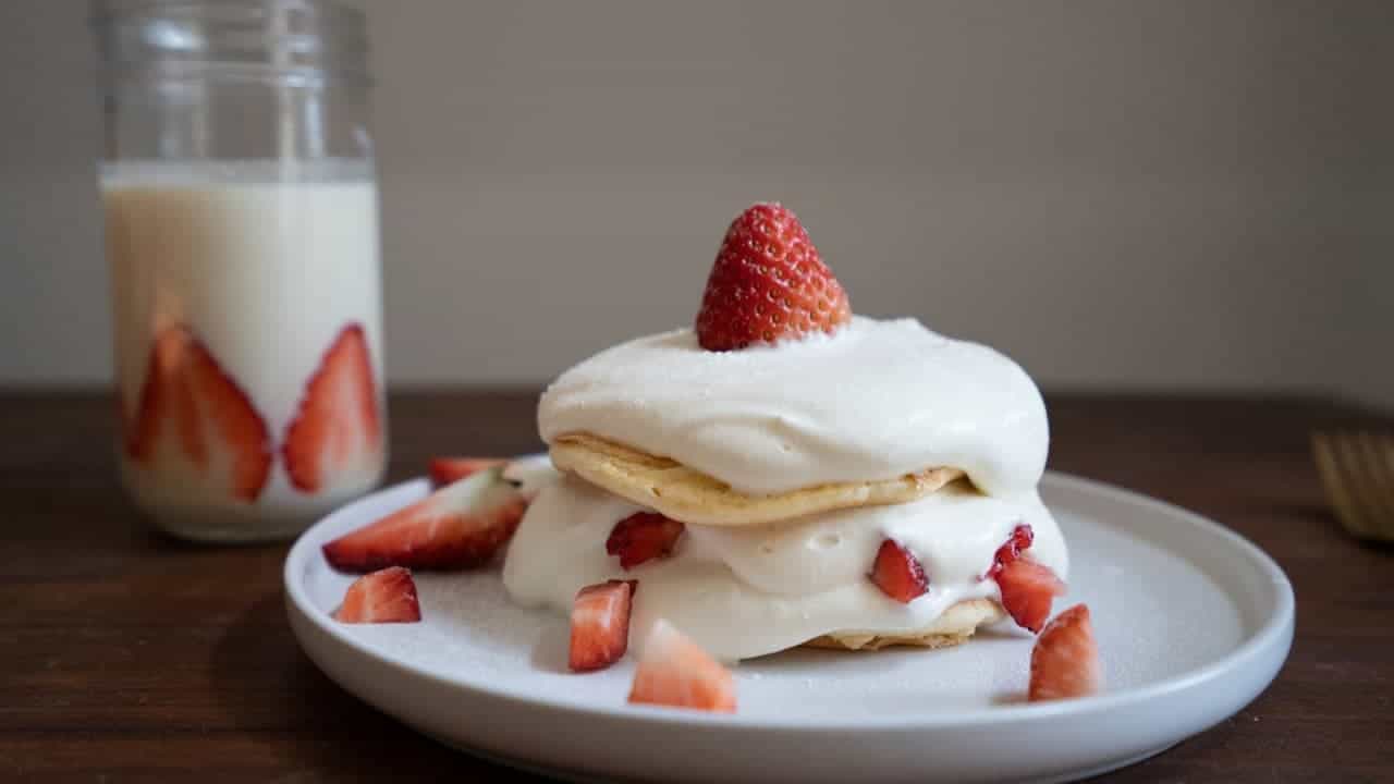 Strawberry shortcake dessert on white plate with whipped cream and fresh berries, alongside glass of milk with strawberries
