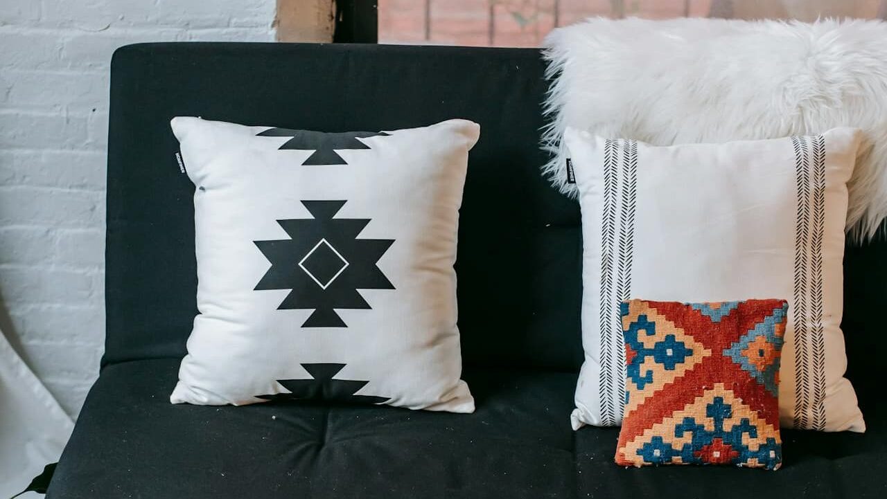 Black sofa with southwestern-inspired pillows: white with geometric pattern, white with stripes, small colorful kilim, and faux fur throw