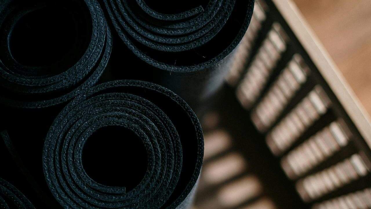 Close-up of tightly rolled black yoga mats placed vertically inside a slatted storage basket, showing the textured surface and spiral shape of each mat